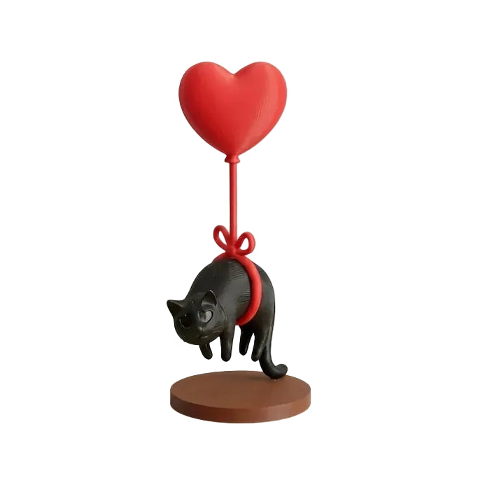 Figurine chat flottant avec ballon cœur rouge, chat noir suspendu par une corde rouge sur socle marron.